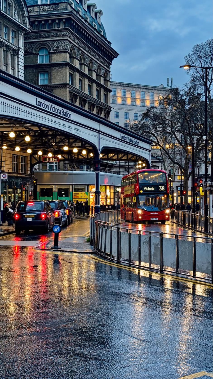 A red bus and black cabs outside London Victoria Station in the rain